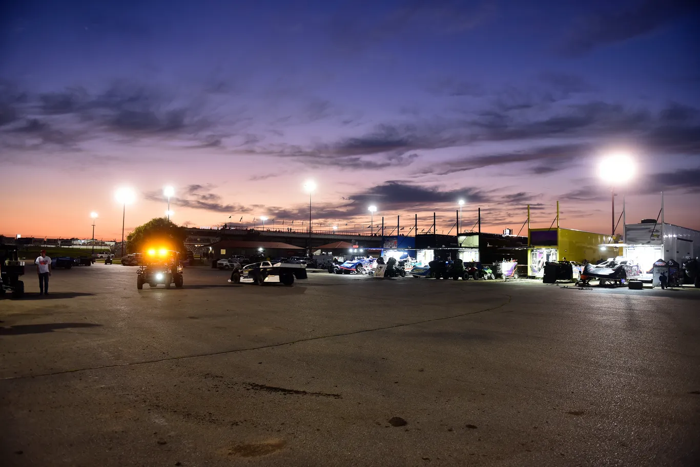 Pit lane at sunset, haulers lit up and cars being readied for the feature