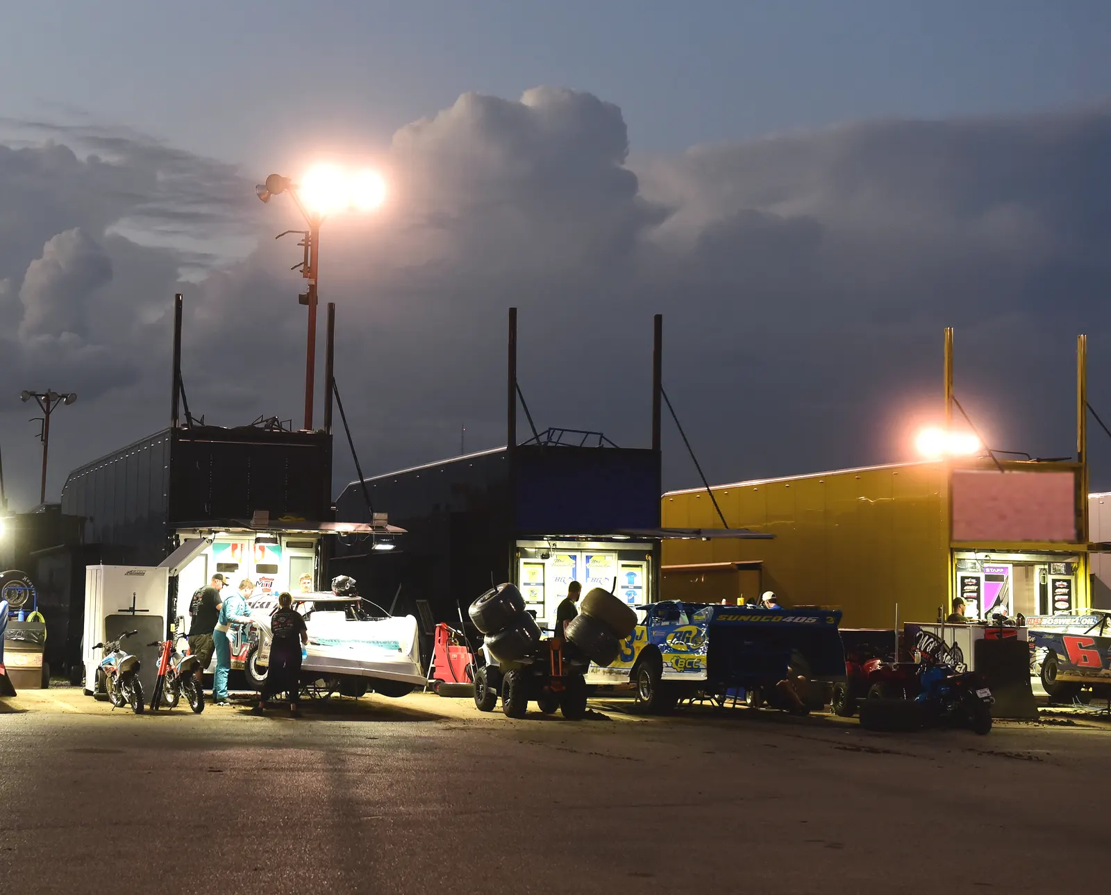 Crews working under the awning lights in the pits at dusk